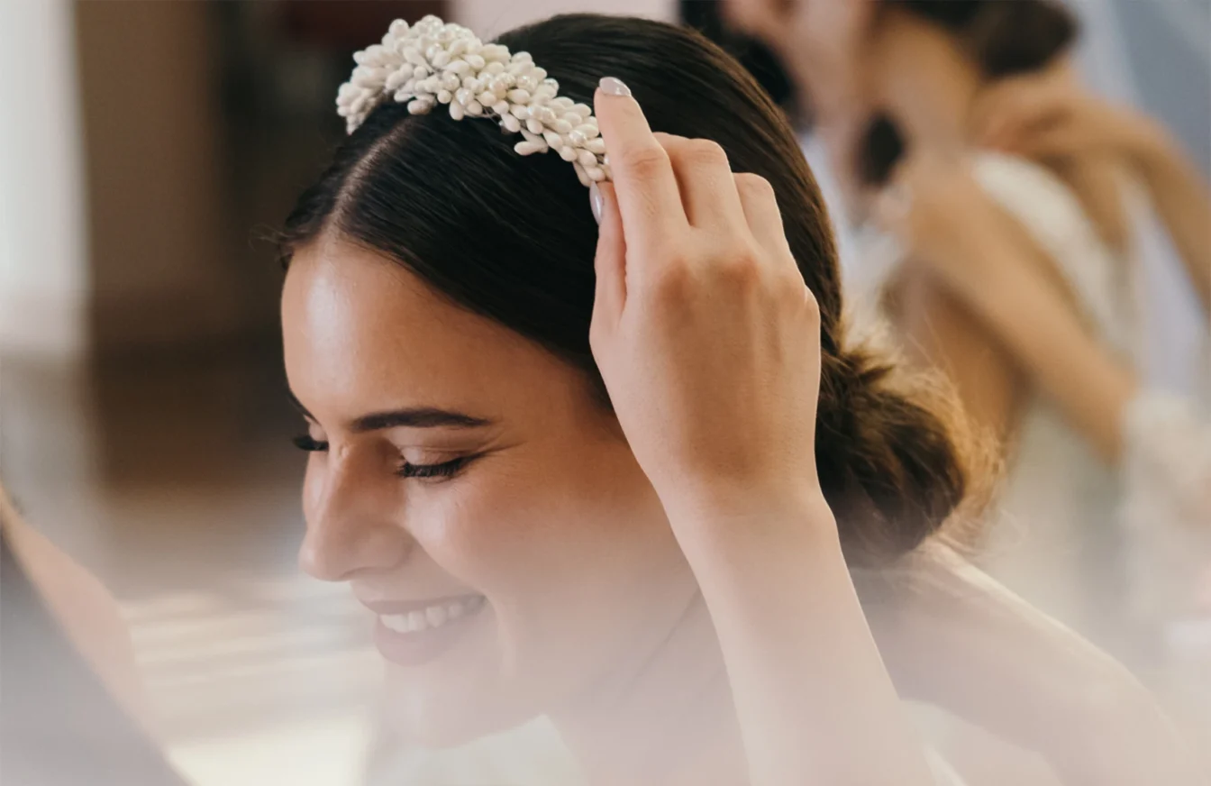 Novia feliz y sonriente con el pelo liso recogido mientras le colocan una diadema en el pelo
