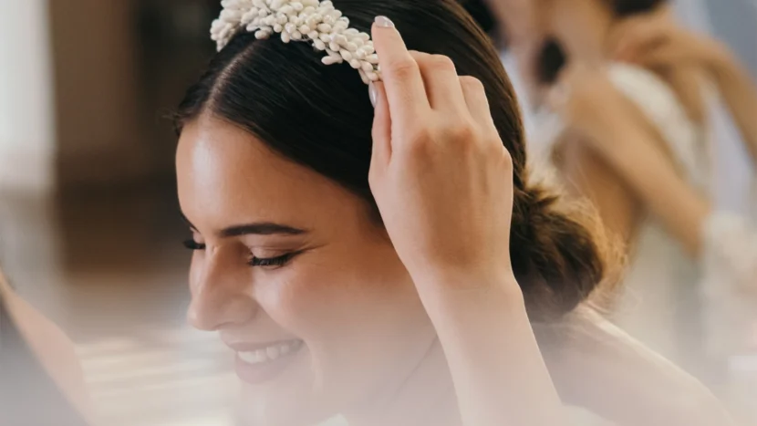 Imagen de una novia feliz y sonriente con el pelo liso recogido mientras le colocan una diadema en el pelo